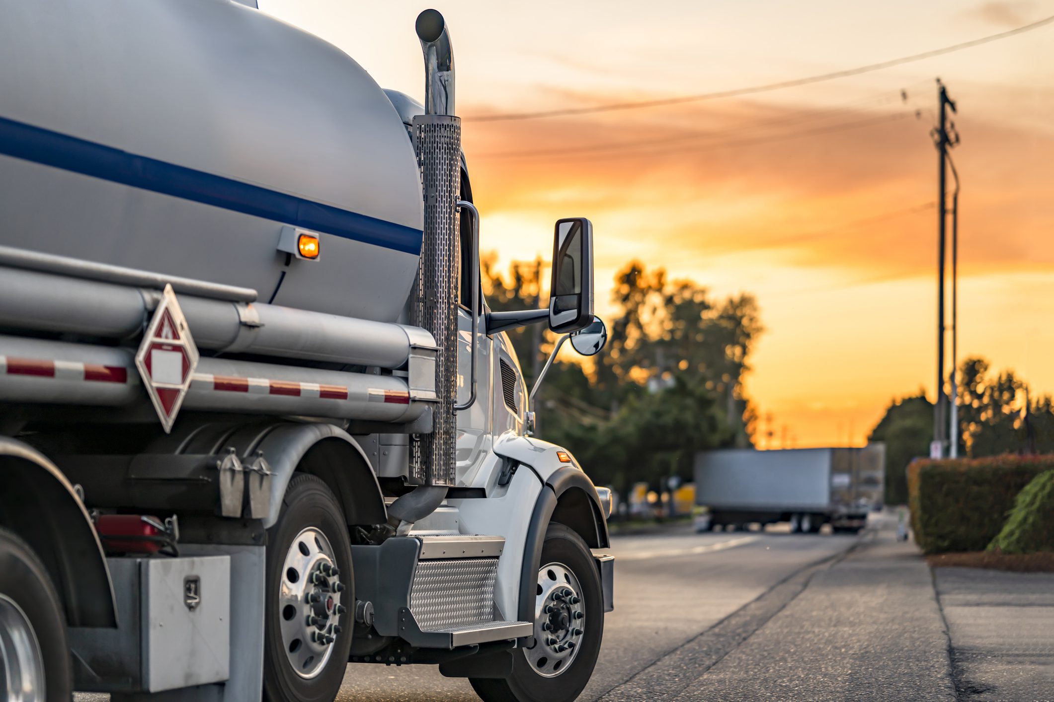Industrial carrier white day cab big rig semi truck tractor transporting flammable fuel liquid in tank semi trailer running on the local road at evening sunset time